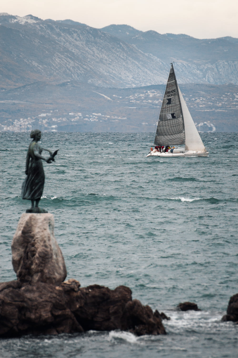 a statue of a woman on a rock with a sailboat in the background
