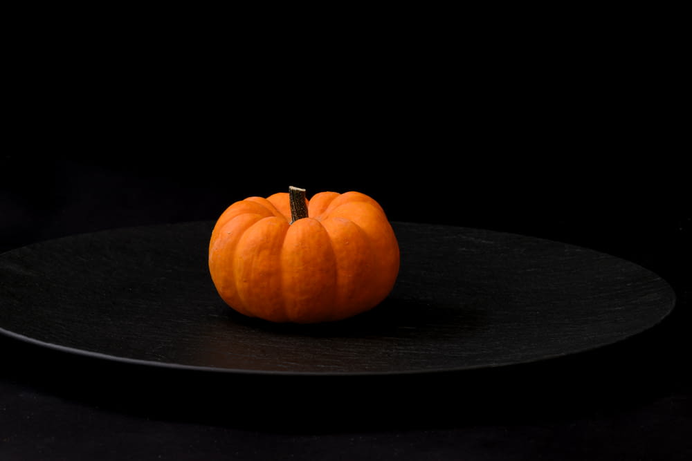 a small orange pumpkin sitting on a black plate