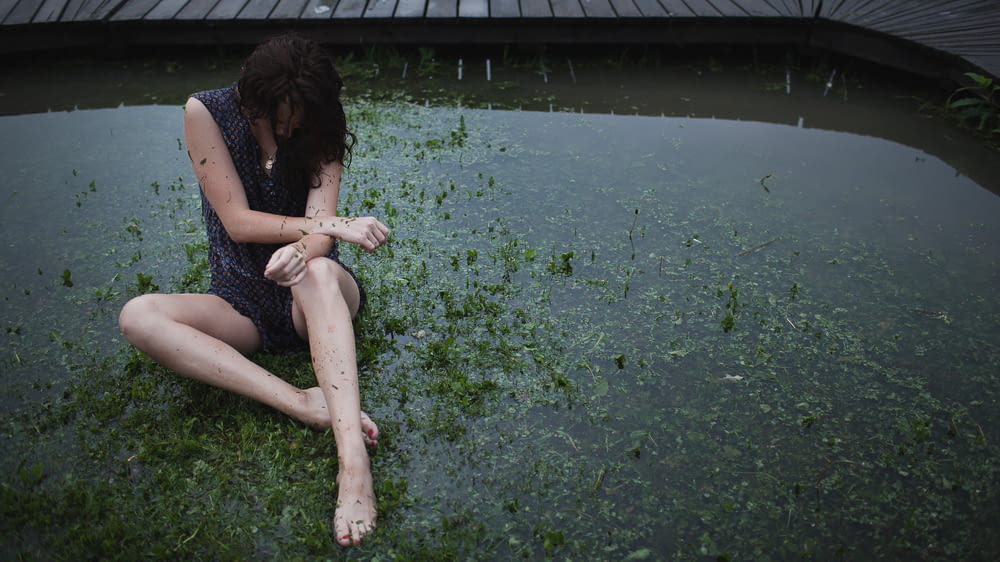 a woman sitting on the ground next to a body of water