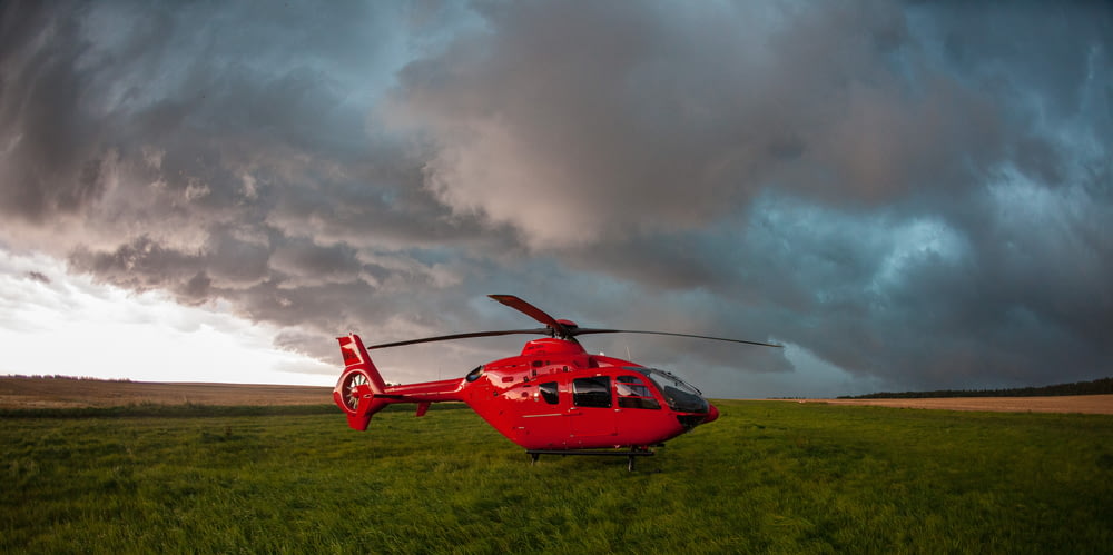 a red helicopter sitting on top of a lush green field