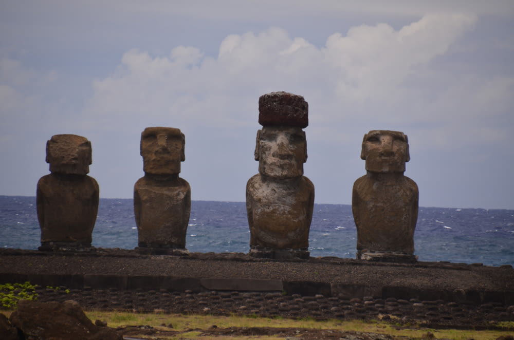 a row of statues sitting on top of a cliff near the ocean