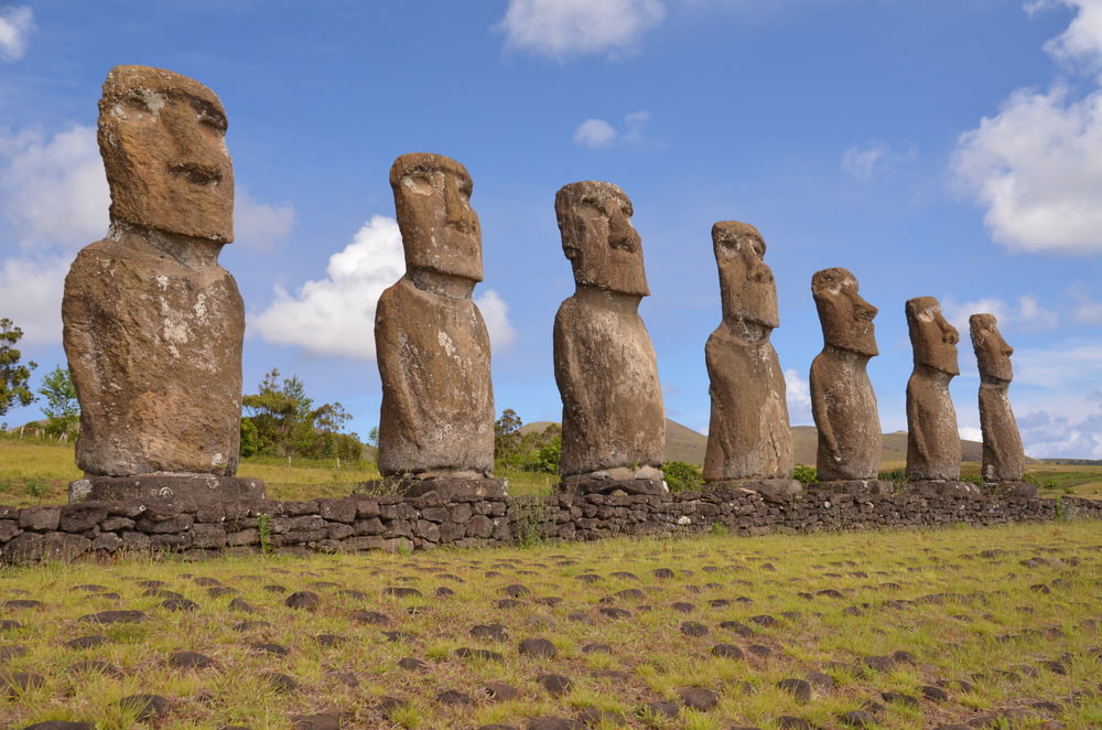 a row of moai statues sitting on top of a grass covered field