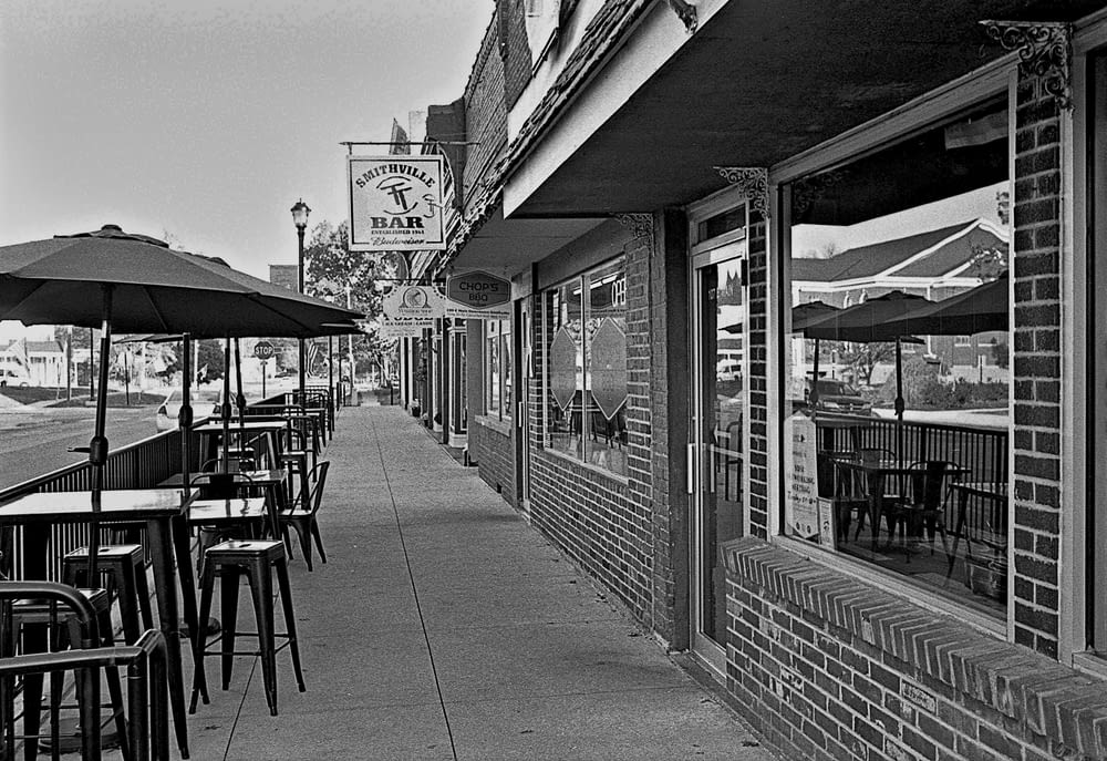 a sidewalk lined with tables and chairs next to a building