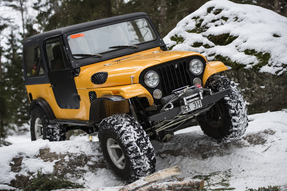 a yellow jeep driving down a snow covered road