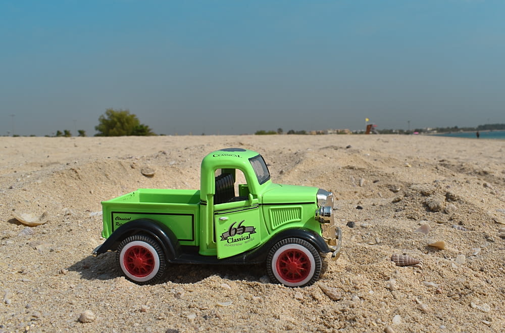 a green toy truck sitting on top of a sandy beach