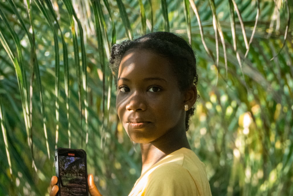 a young girl holding a cell phone in front of a palm tree