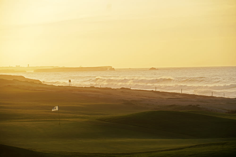 the sun is setting over the ocean and a golf course