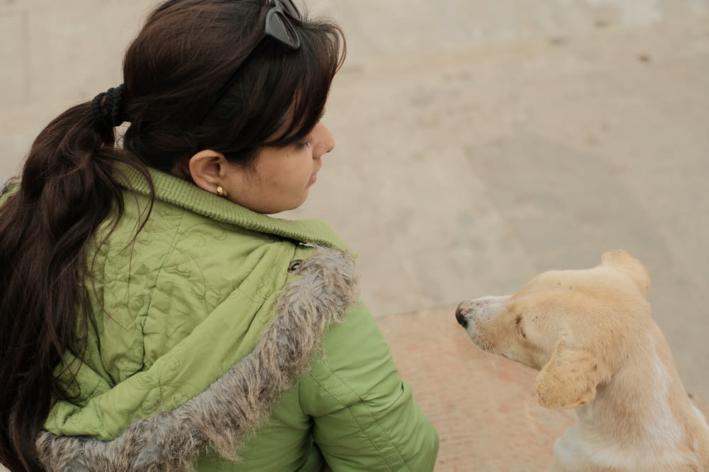 a woman in a green jacket petting a dog