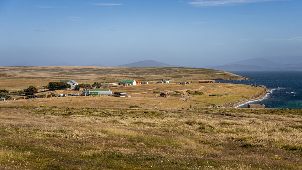 a grassy field with houses and a body of water in the distance