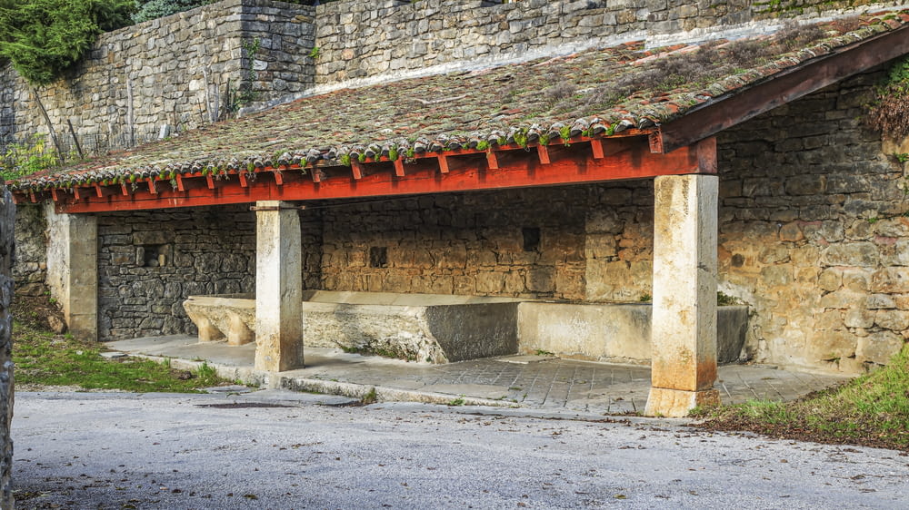a stone building with a red roof and a bench