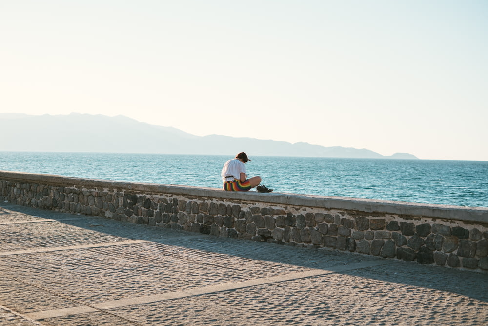 a man sitting on a stone wall next to the ocean