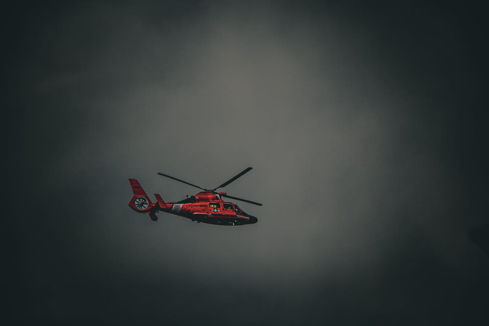 a red helicopter flying through a cloudy sky