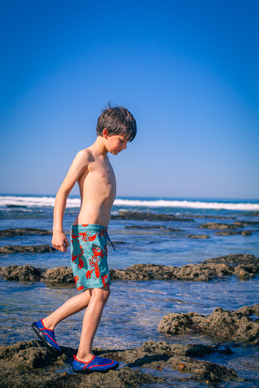 a young boy standing on top of a rock covered beach