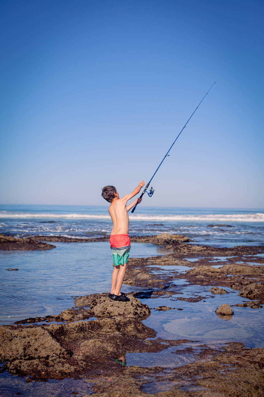 a young boy standing on top of a rocky beach holding a fishing pole