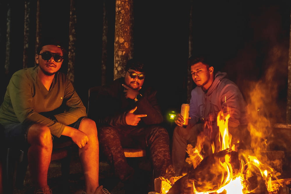 three men sitting around a campfire at night