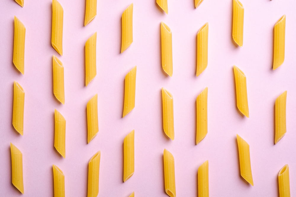 a pink background with yellow pieces of pasta