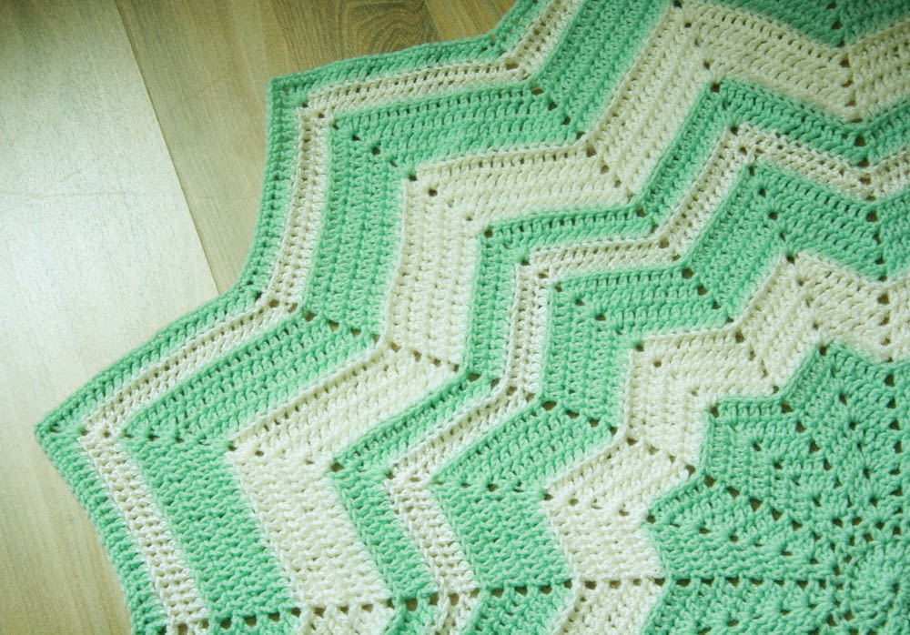 a green and white crocheted blanket on a wooden floor
