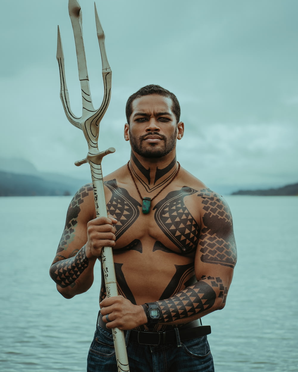 a man with tattoos holding a large spear