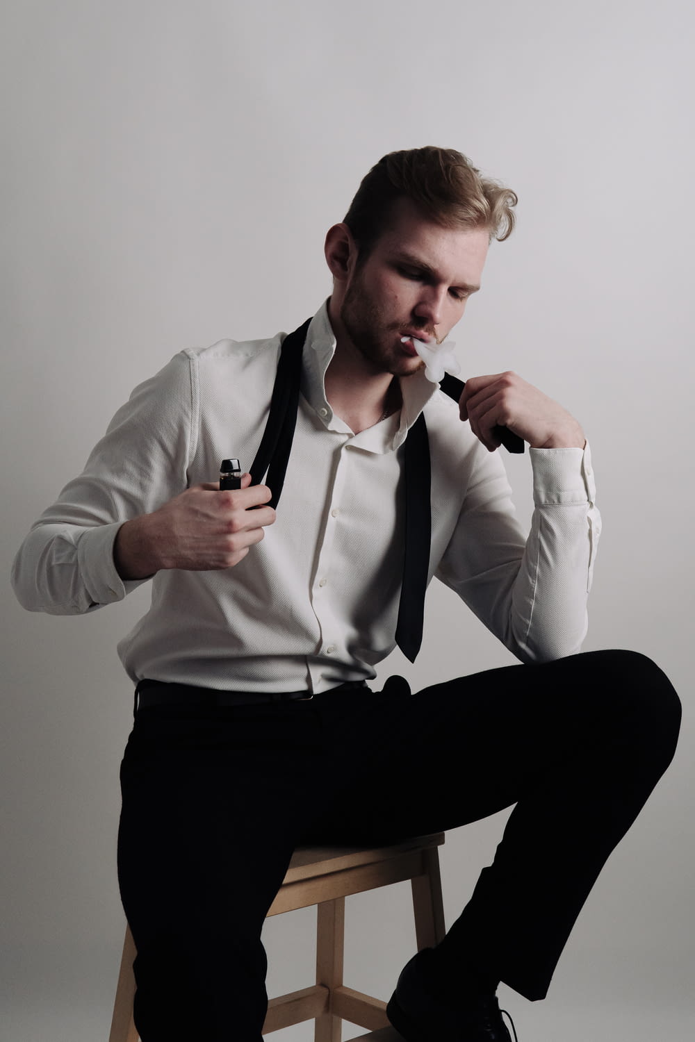 a man in a white shirt and black tie sitting on a stool