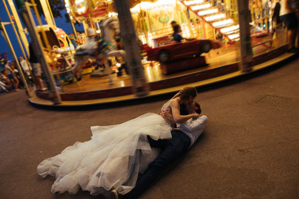 a bride and groom laying on the ground in front of a carousel