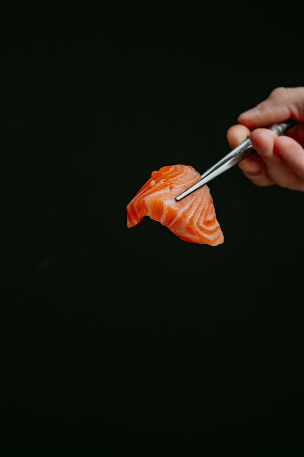 a person cutting a piece of salmon with a pair of tongs
