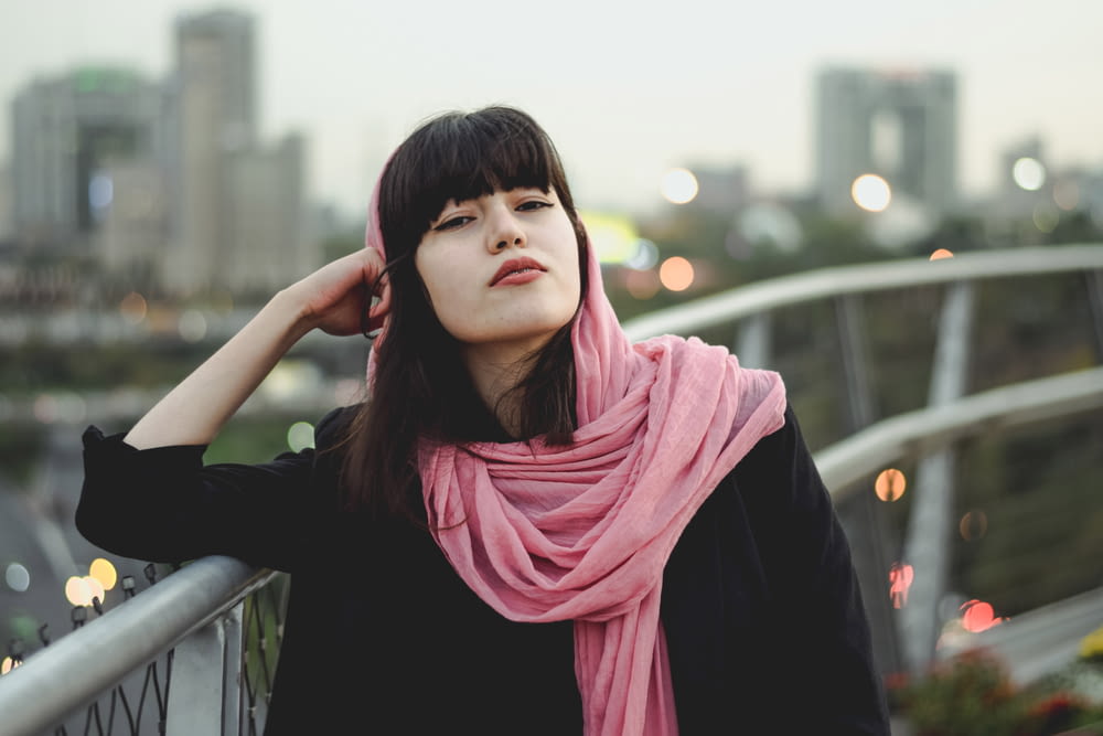 a woman wearing a pink scarf standing on a bridge