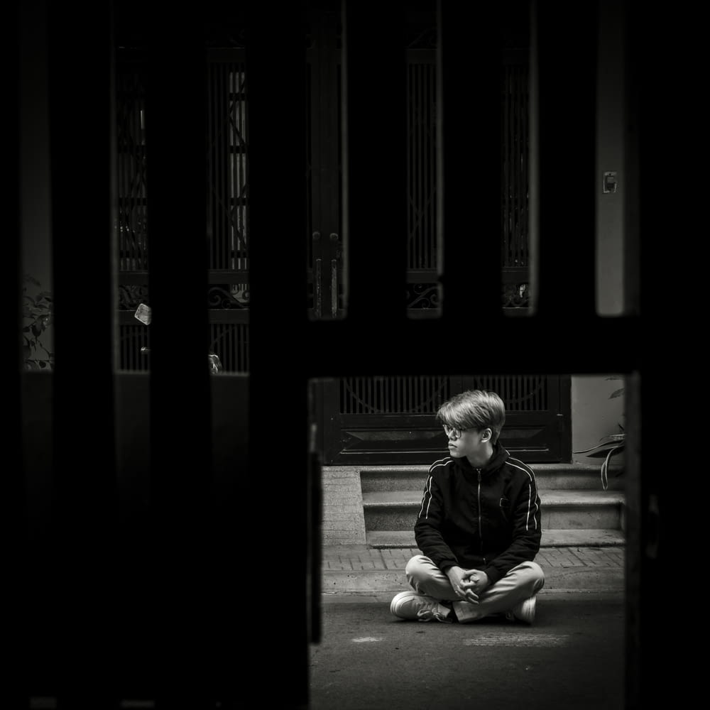 a young boy sitting on the ground in front of a door