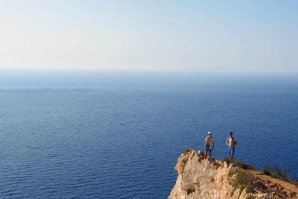 two people standing on a cliff overlooking the ocean