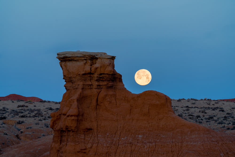 a full moon rises over a desert landscape