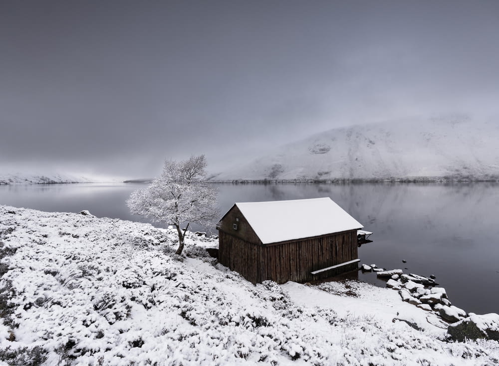 a small cabin on the shore of a lake covered in snow