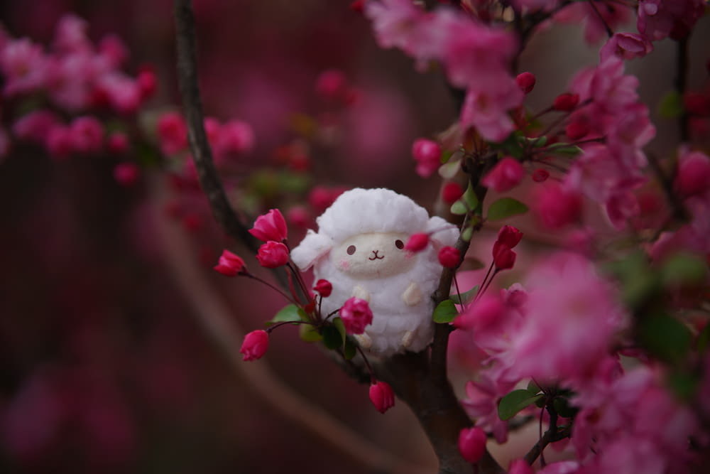 a stuffed animal is sitting on a branch of a flowering tree