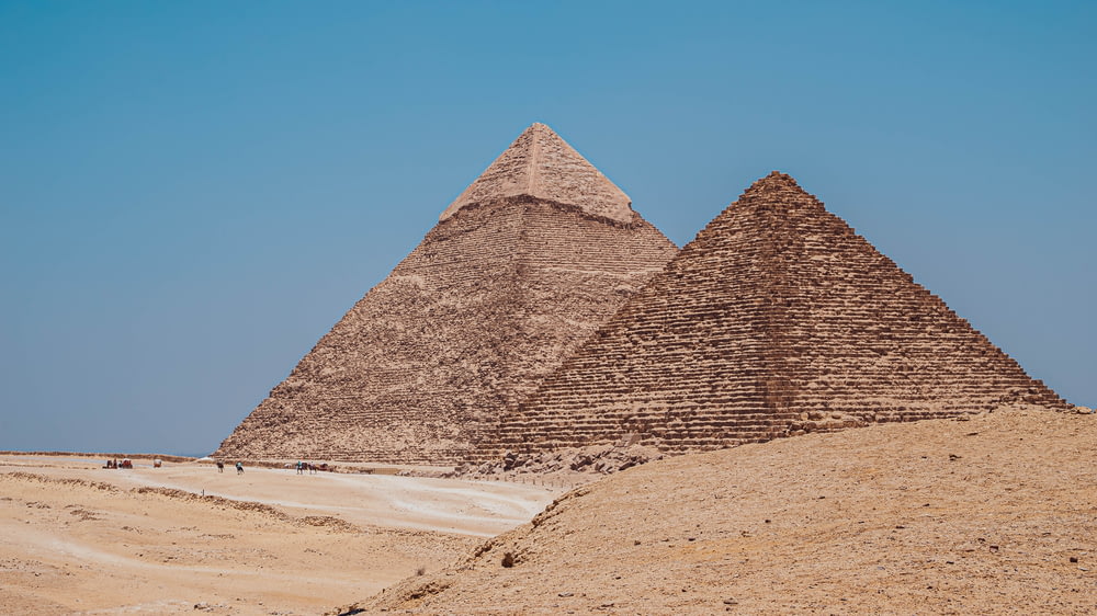 two pyramids in the desert with a blue sky in the background