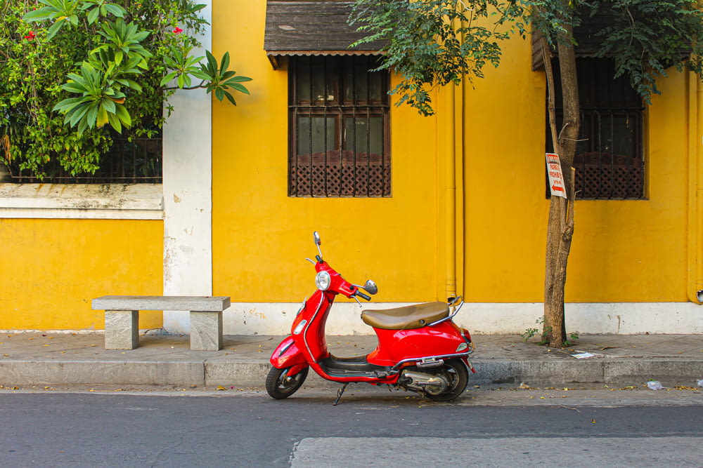 a red scooter parked next to a yellow building