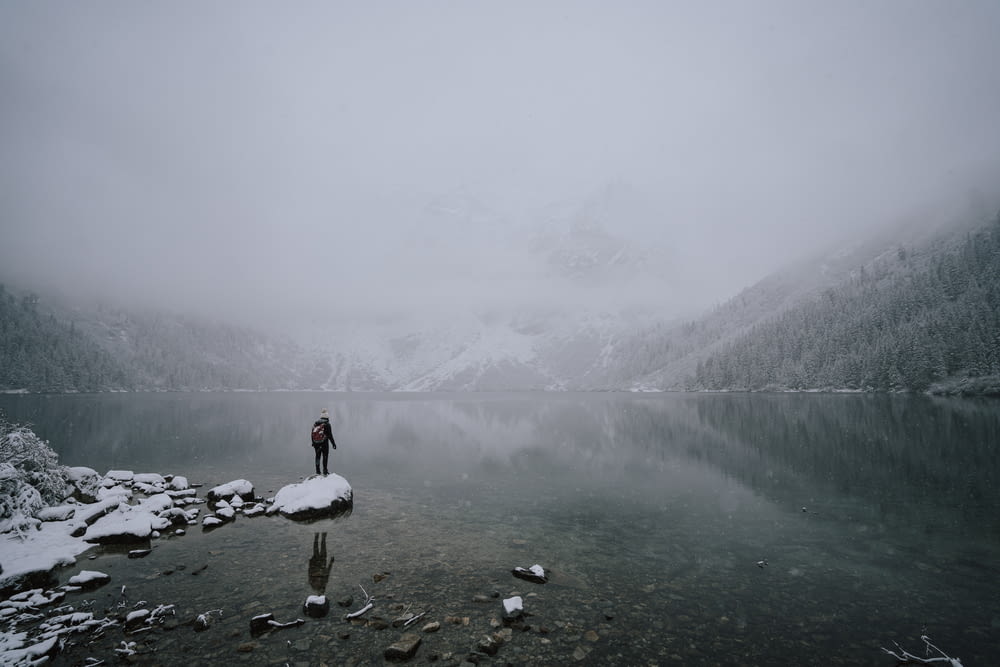 uma pessoa de pé à beira de um lago cercado por montanhas