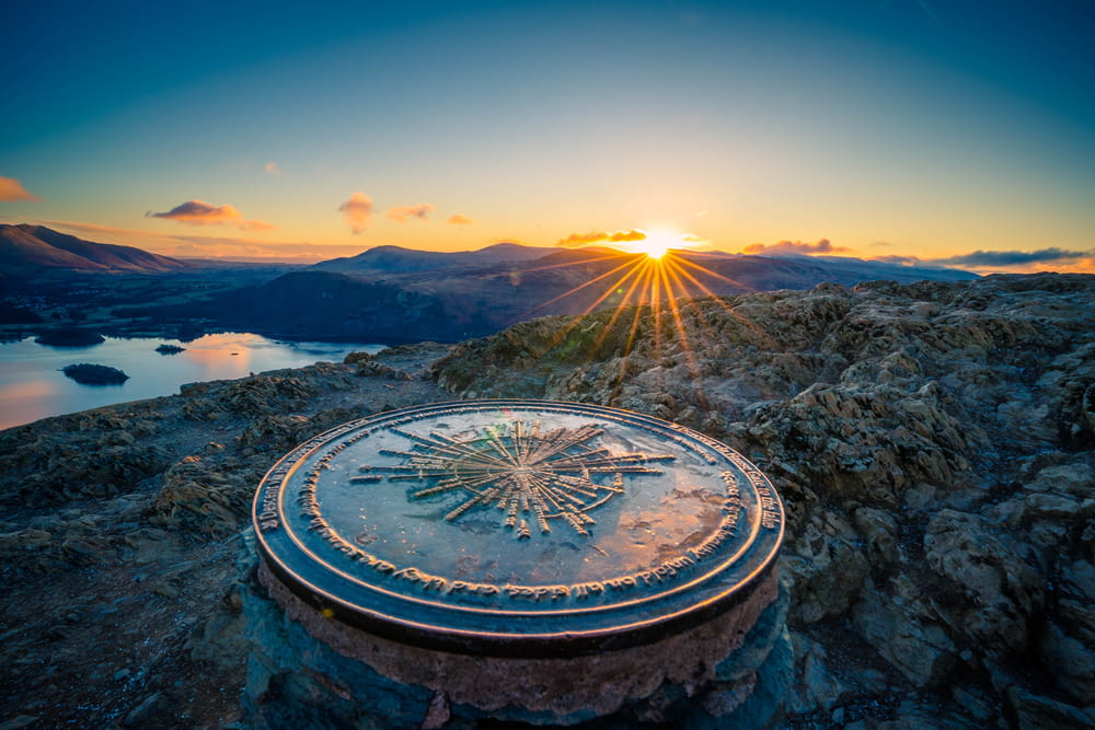 a sun setting over a mountain with a clock on it