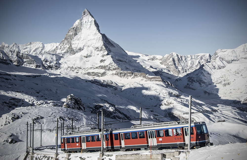a red and blue train traveling past a snow covered mountain