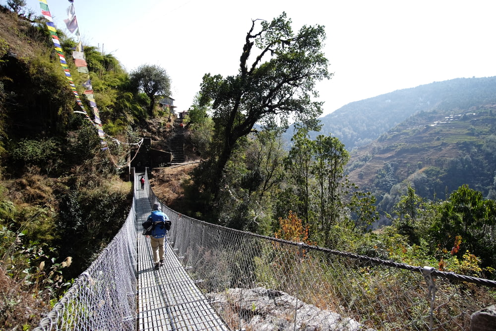 a man walking across a suspension bridge in the mountains