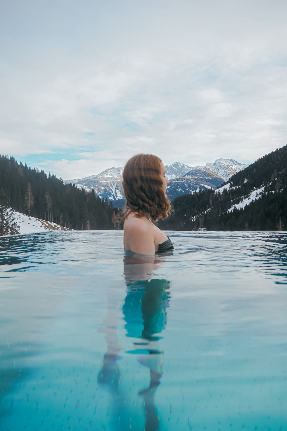 a woman sitting in a pool of water with mountains in the background