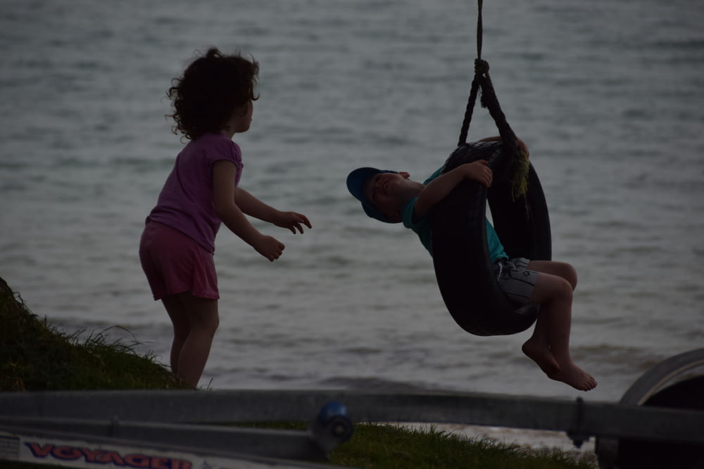 a little girl standing next to a little boy on a swing