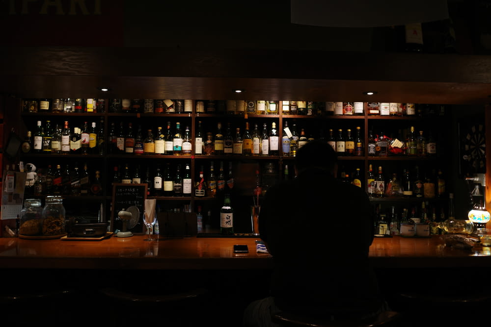 a man sitting at a bar with a lot of bottles behind him