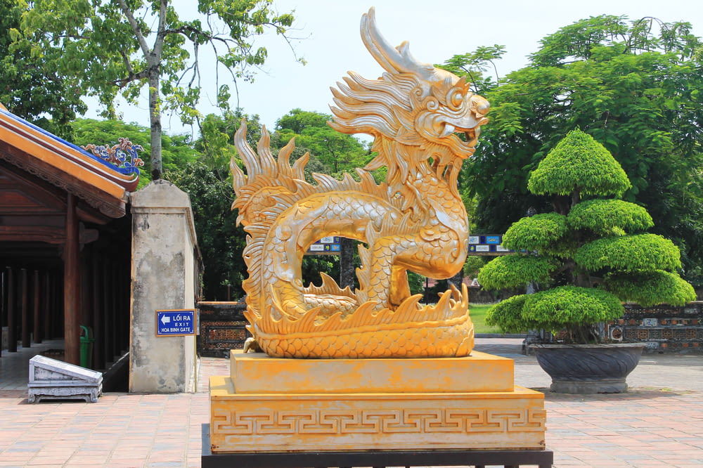 a golden dragon statue in a park setting