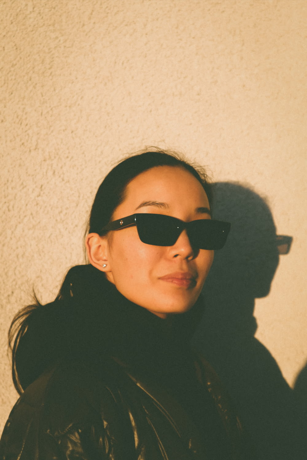 a woman wearing sunglasses standing next to a wall
