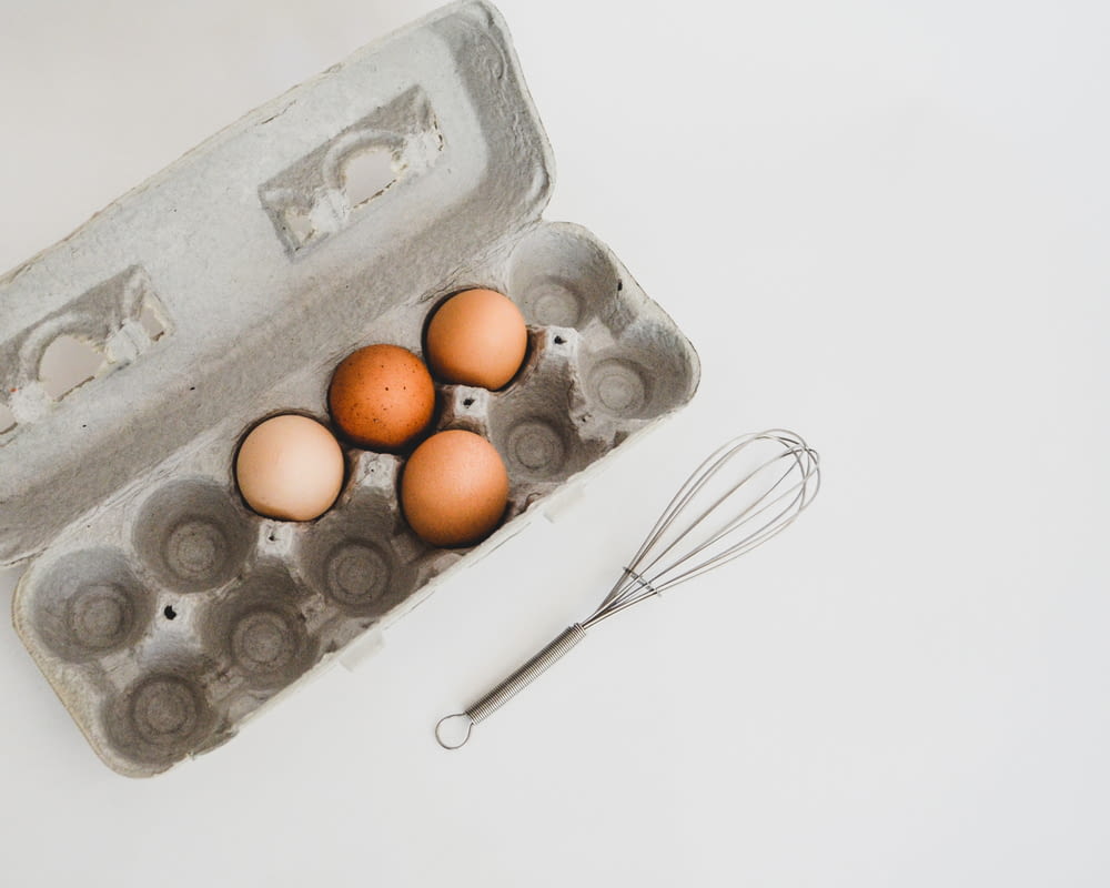 a carton of eggs and a whisk on a table