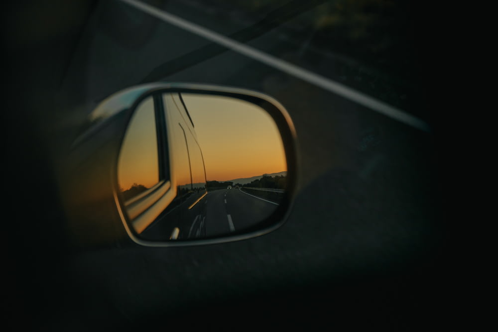 a rear view mirror reflecting a sunset on a highway