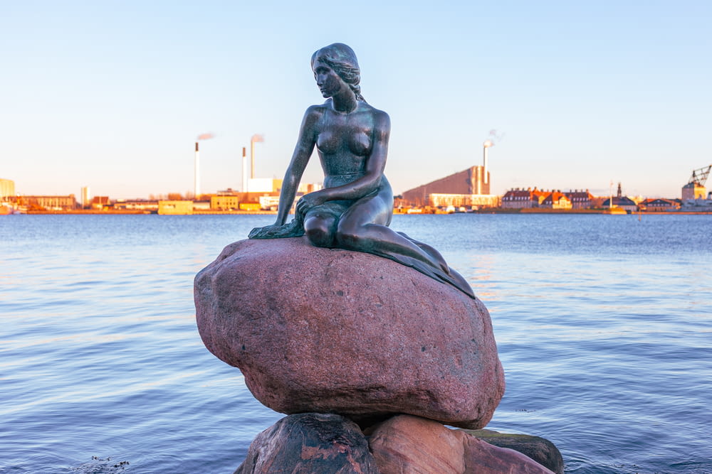 Una statua di una donna seduta sulla cima di una roccia