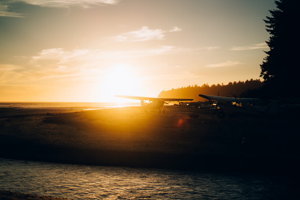 a plane is sitting on the beach at sunset