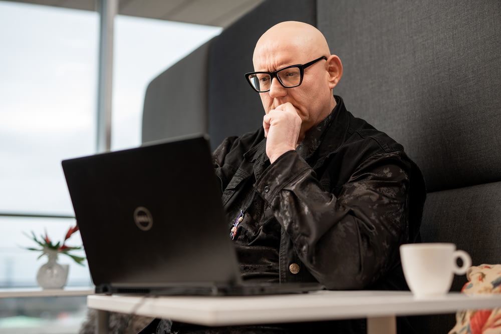 a bald man sitting in front of a laptop computer