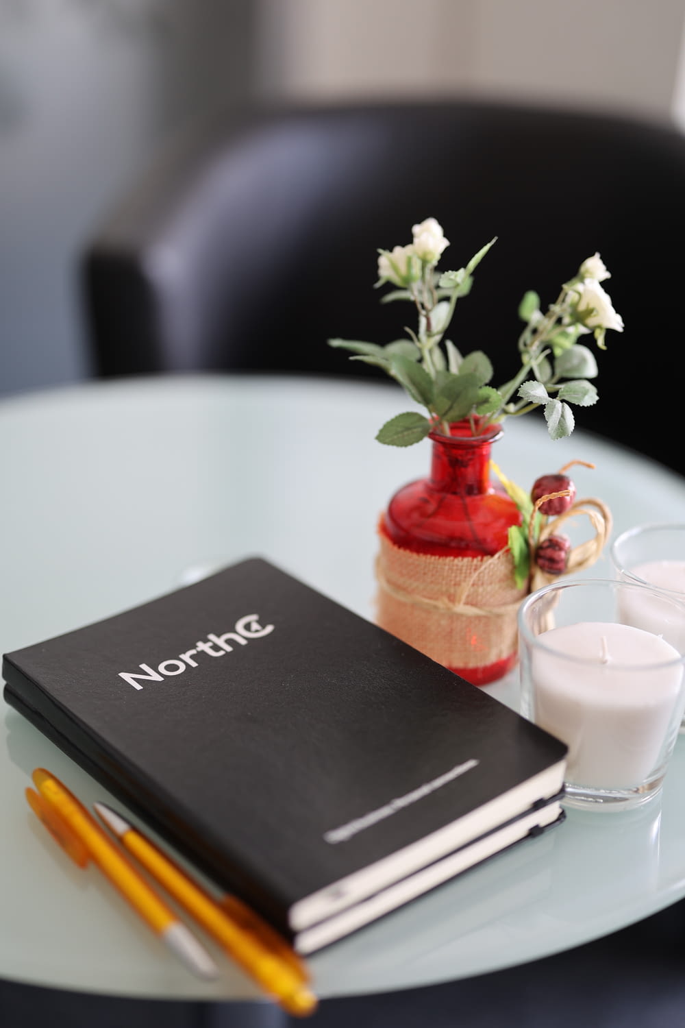a table with a notebook, glass of milk and a vase with flowers on it