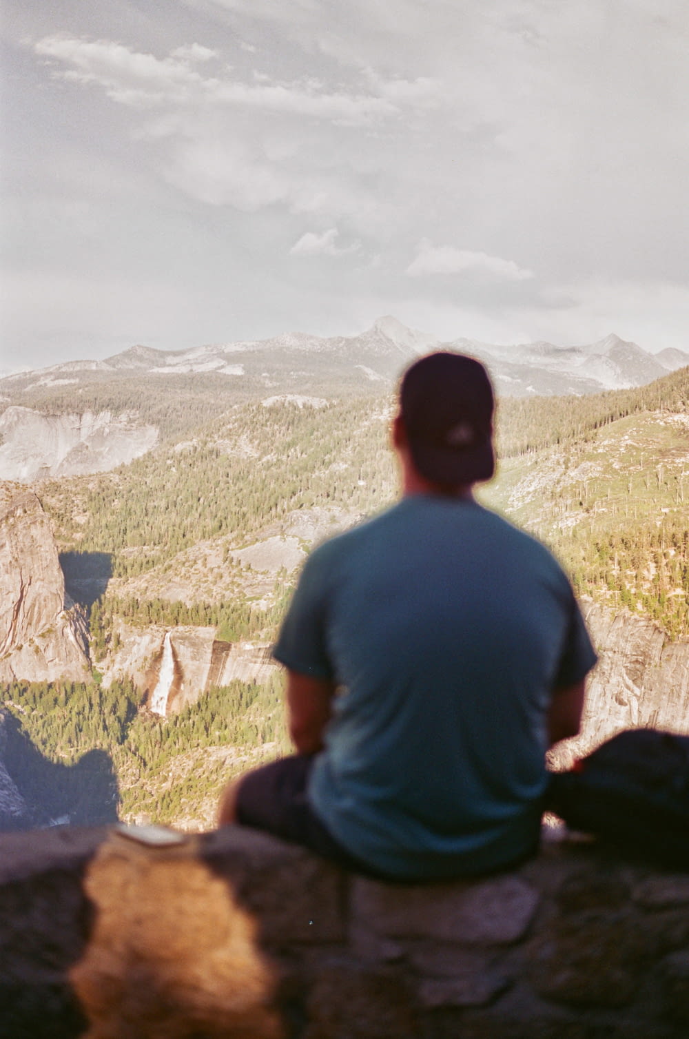 a man sitting on top of a mountain looking at a valley