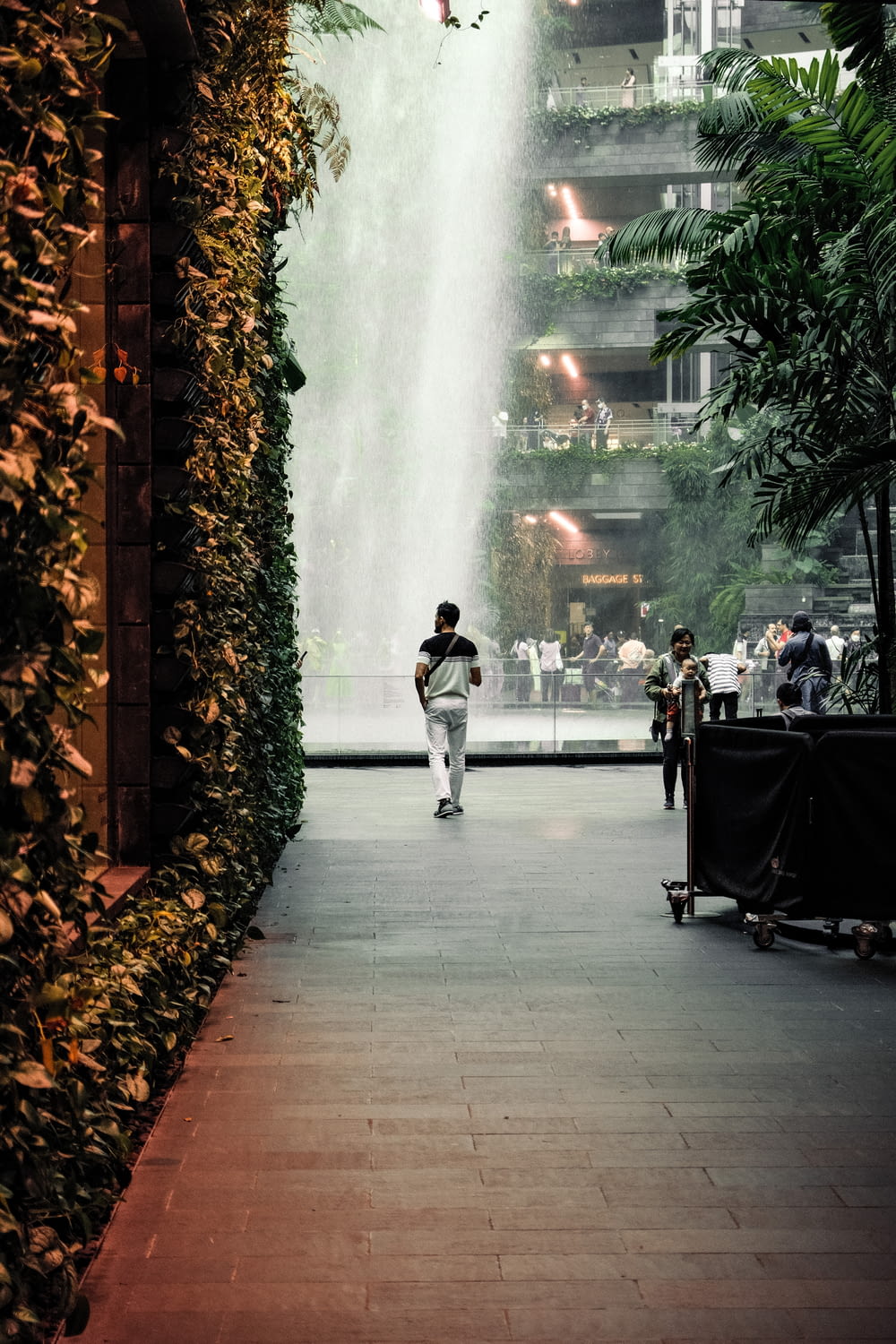 a man walking down a sidewalk next to a tall waterfall